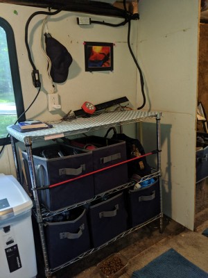Open wire shelves with bins, topped with non-skid shelf liner. The bottom row has tools and bottled water, so it's very heavy and not prone to tipping. The final solution will, of course, be properly attached to the floor/wall. All the electrical will go into conduit, etc.